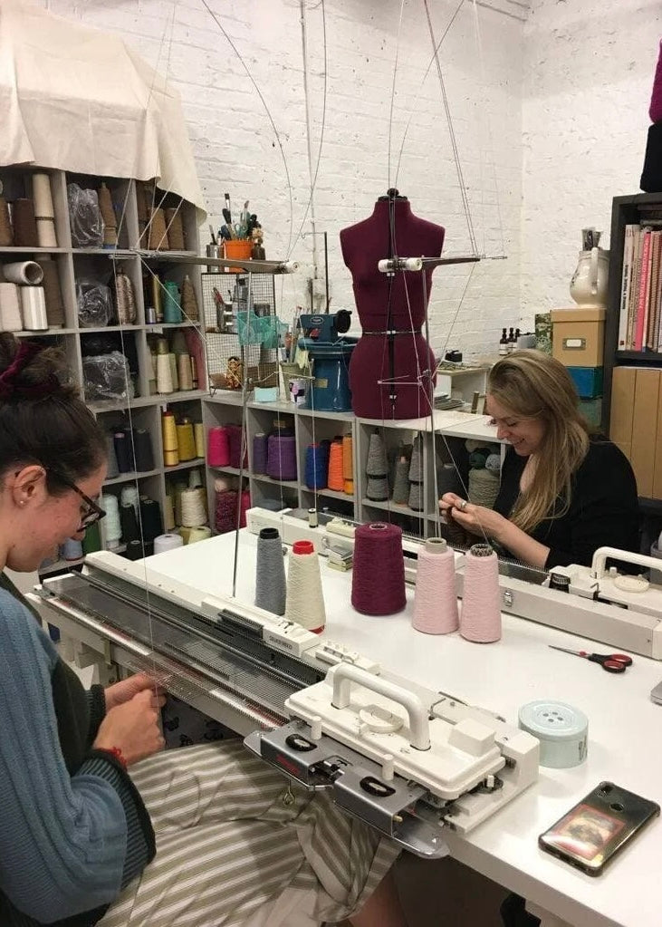 Two women working at a sewing machine in a workshop setting.