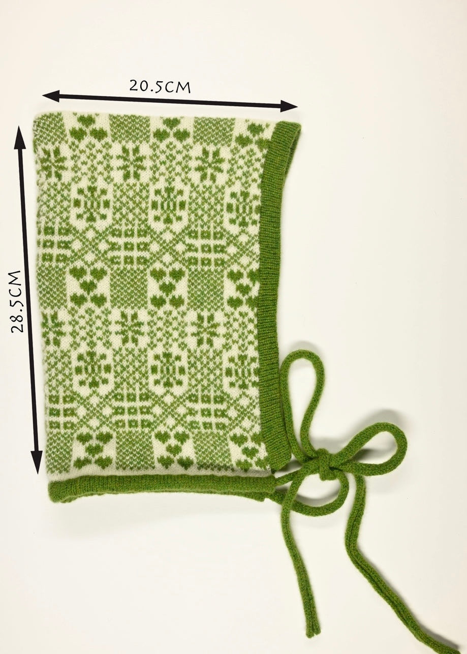 Green knitted bonnet with white fair isle pattern and measurements (28cm long by 20.5cm wide) on a white background