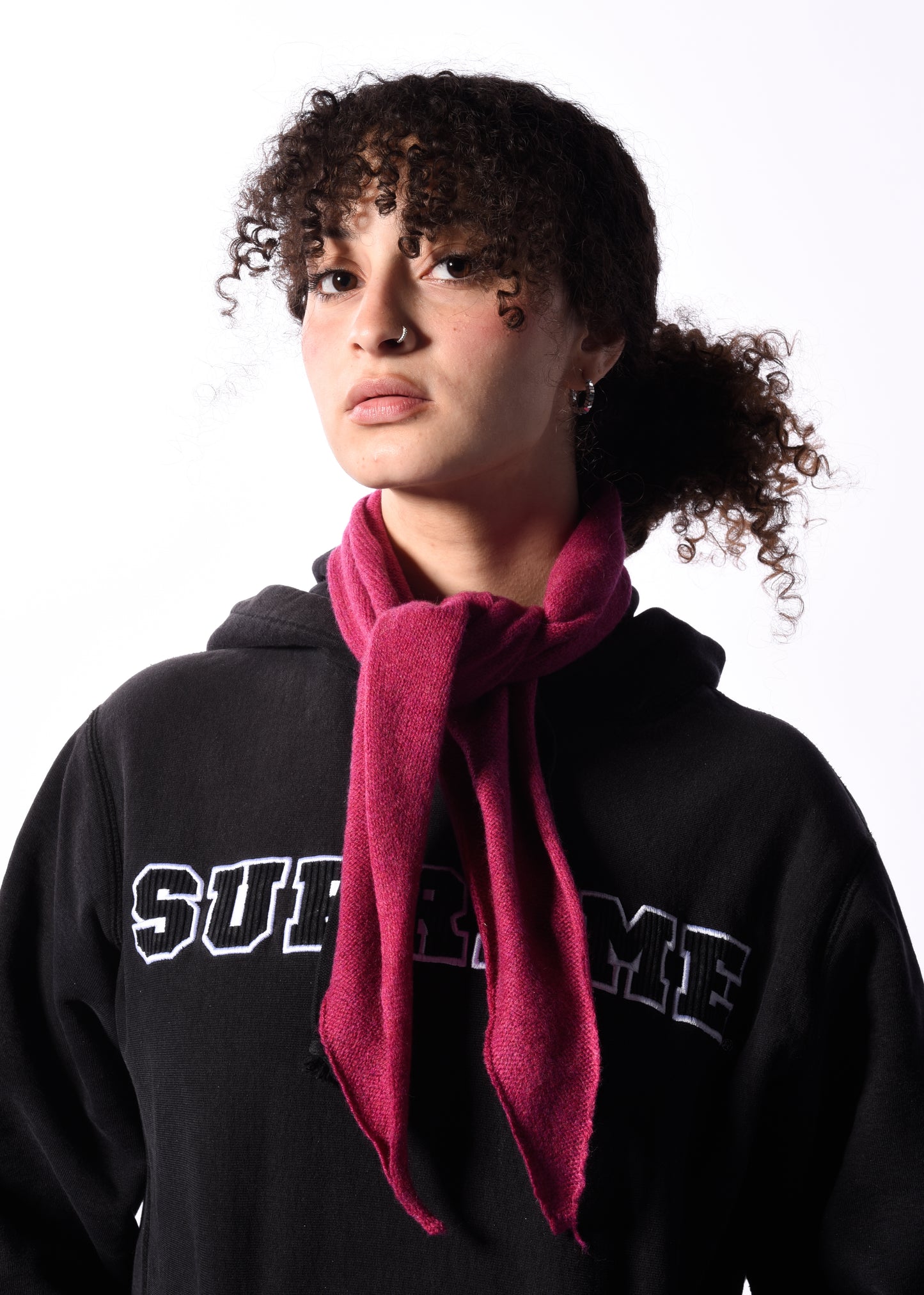 Person wearing a black Supreme hoodie with a pink scarf on a white background