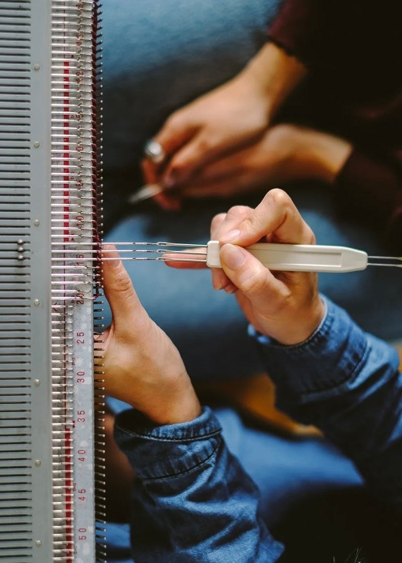Person working with a loom and measuring tool on a blue surface
