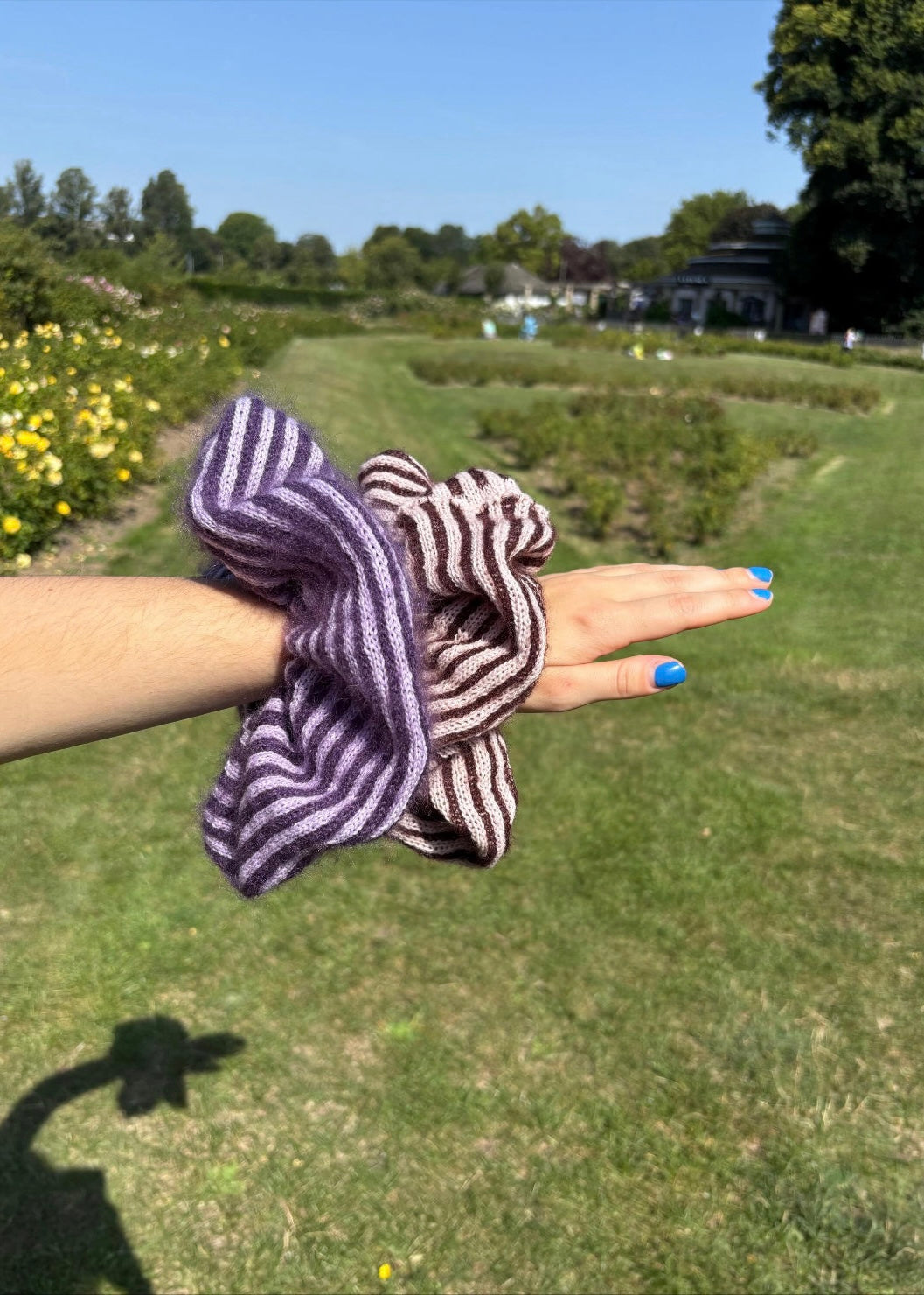 Hand holding a striped scrunchie with a park in the background
