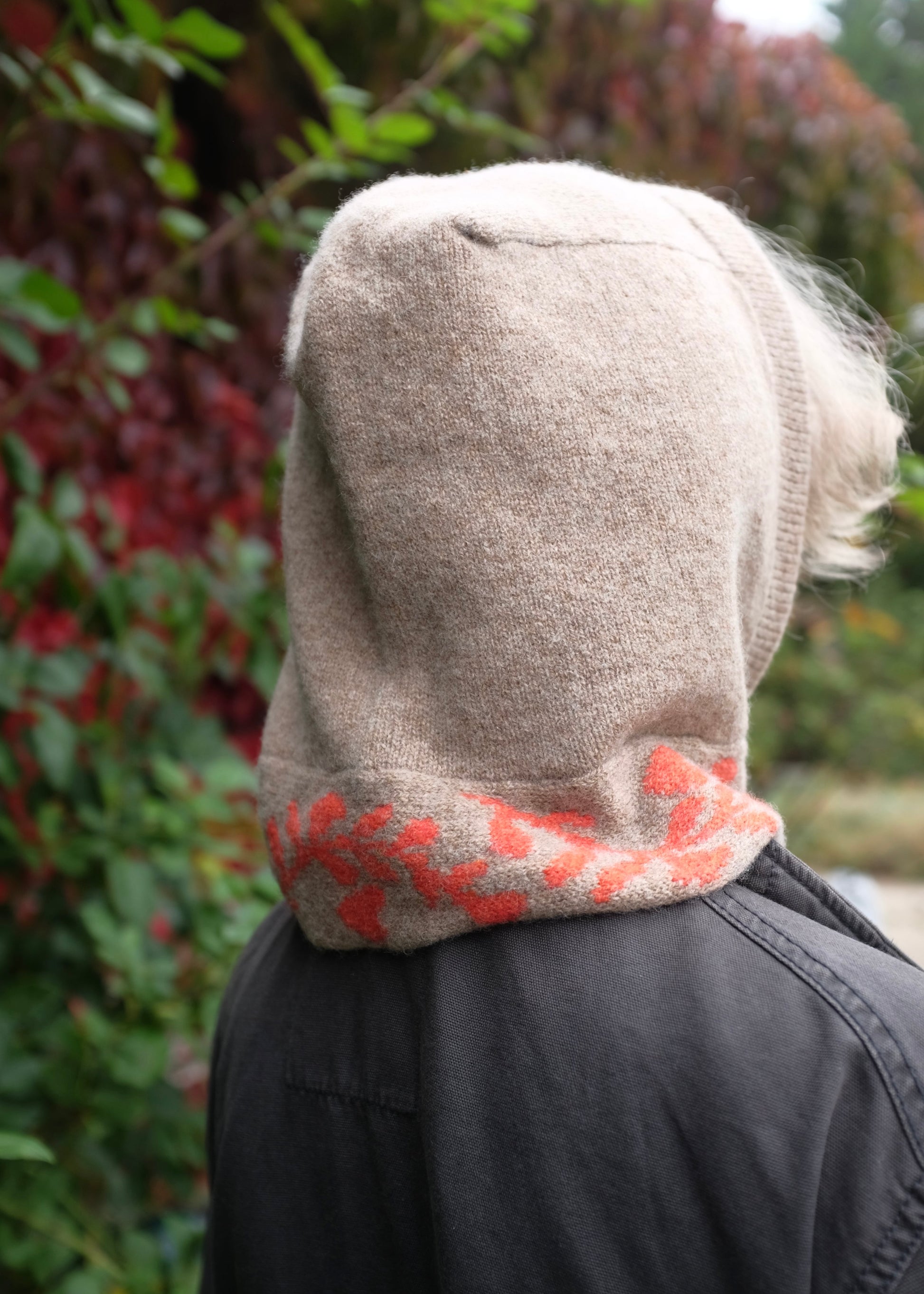 Person wearing a tan knitted hooded garment with a orange  floral pattern in an outdoor setting