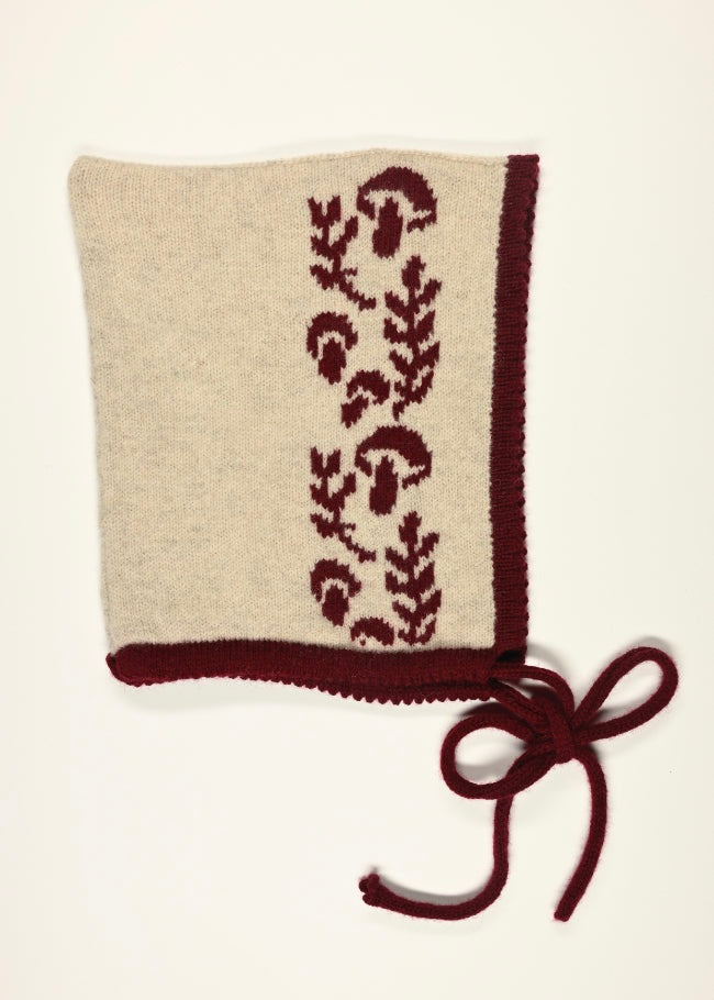 Knitted bonnet with dark red mushroom and leaves pattern on a beige background