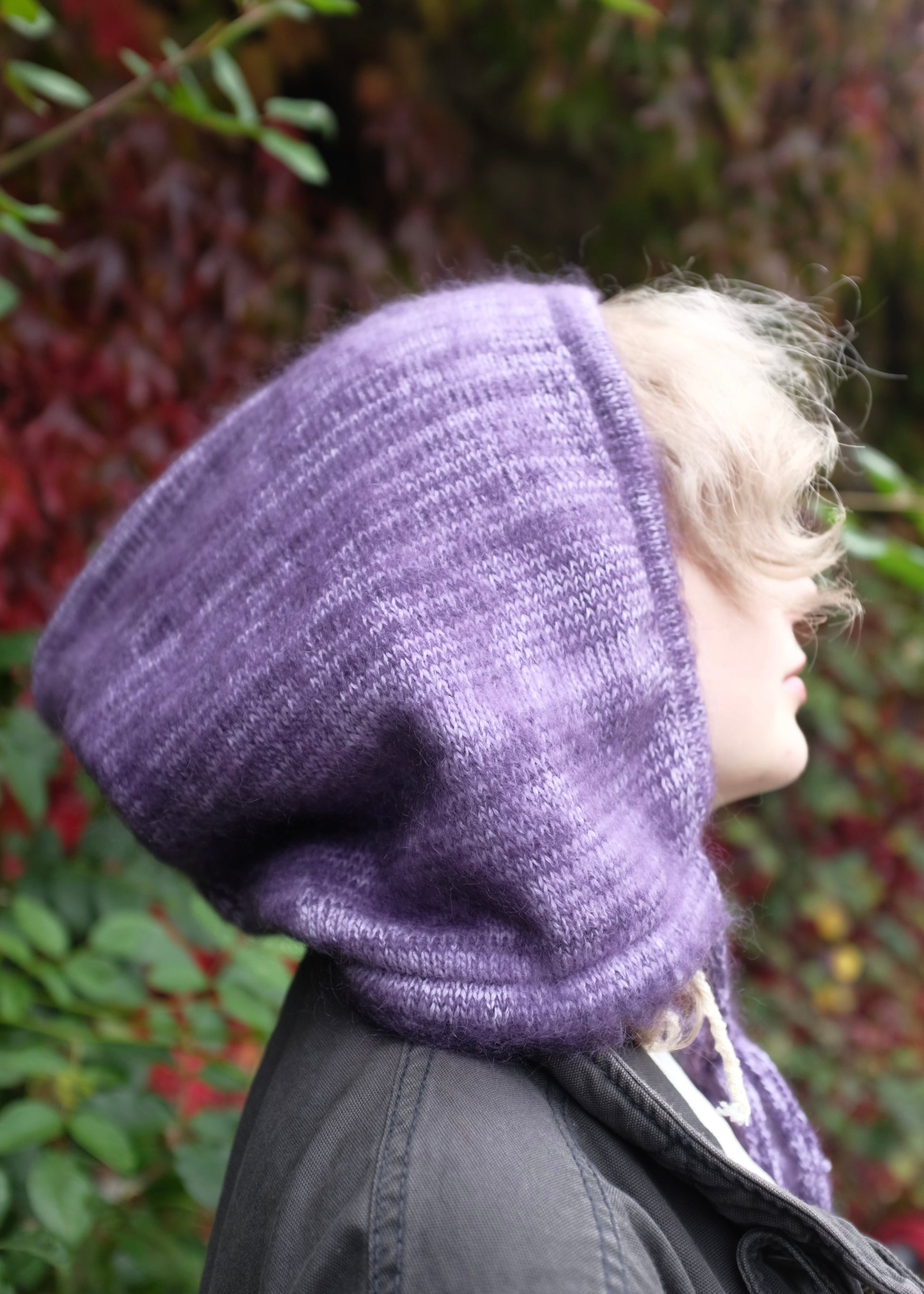 Person wearing a purple knitted hood against a blurred natural background