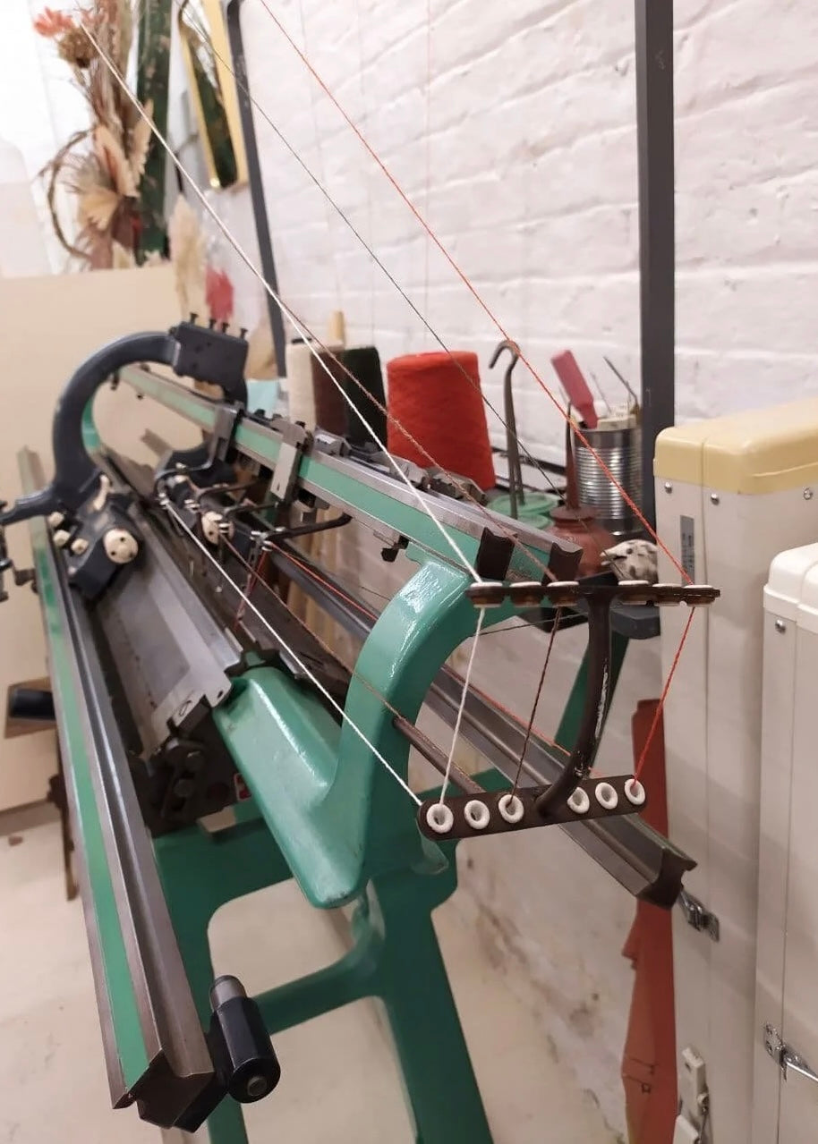 Textile machine with spools of thread against a white brick wall.