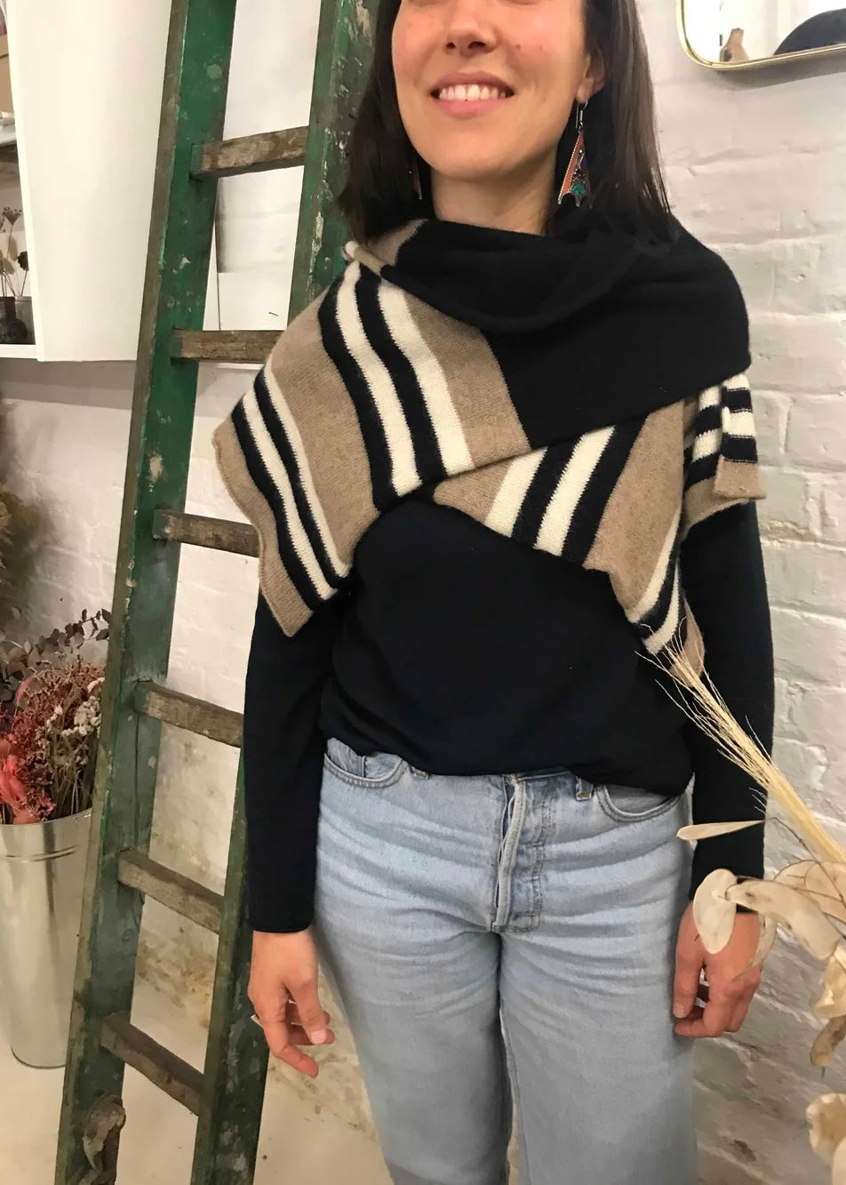 Woman wearing a black turtleneck and knitted striped scarf standing next to a ladder indoors.