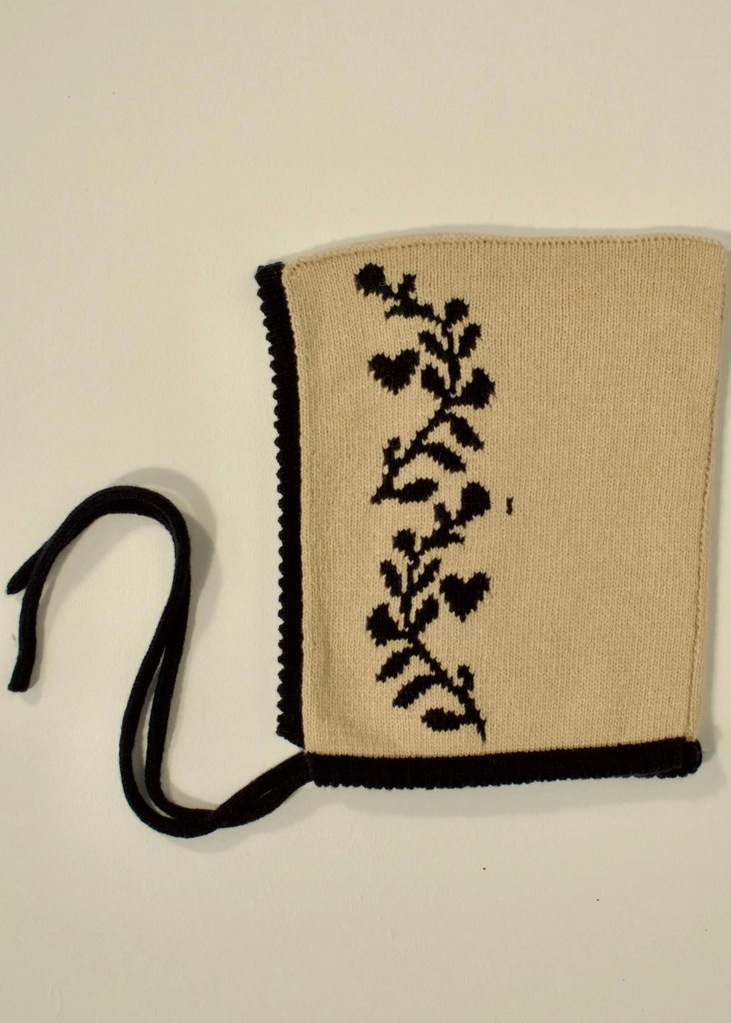 A flat lay of our cashmere knitted bonnet in biege with a navy trim, laurel leaf design and tie 