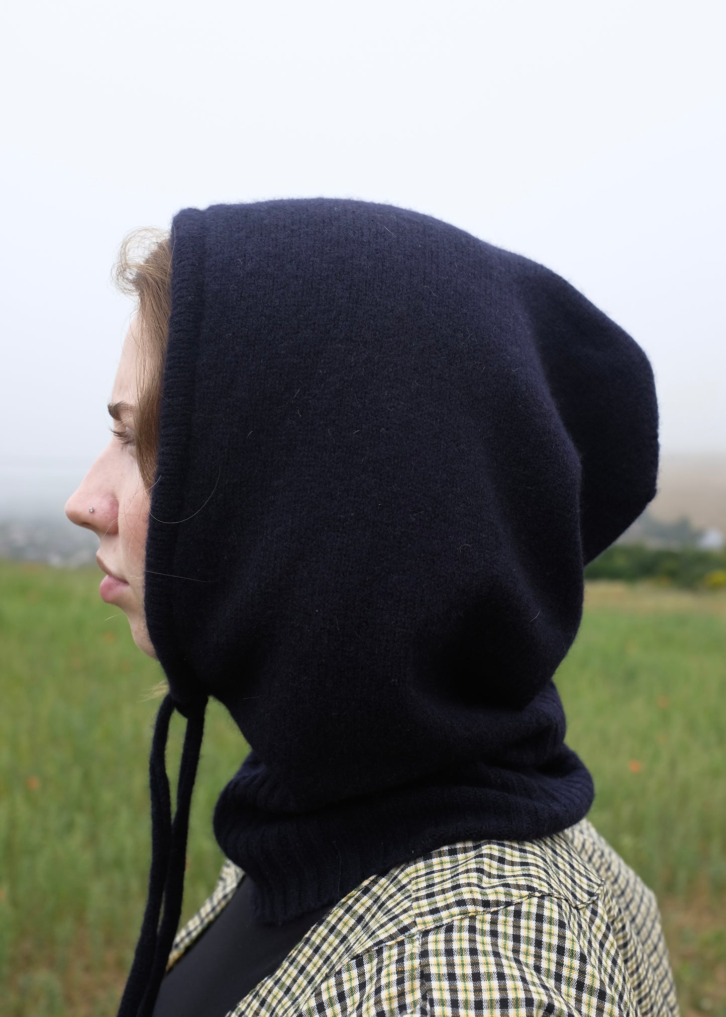 Our cashmere knitted black balaclava hood pictured on a woman from a view outdoors 