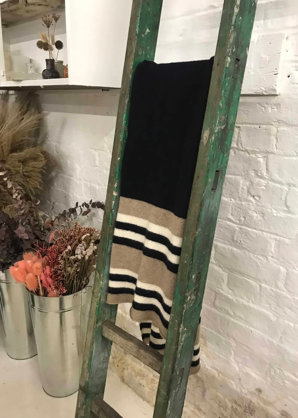Vintage ladder with black and striped knitted scarf against a white brick wall.