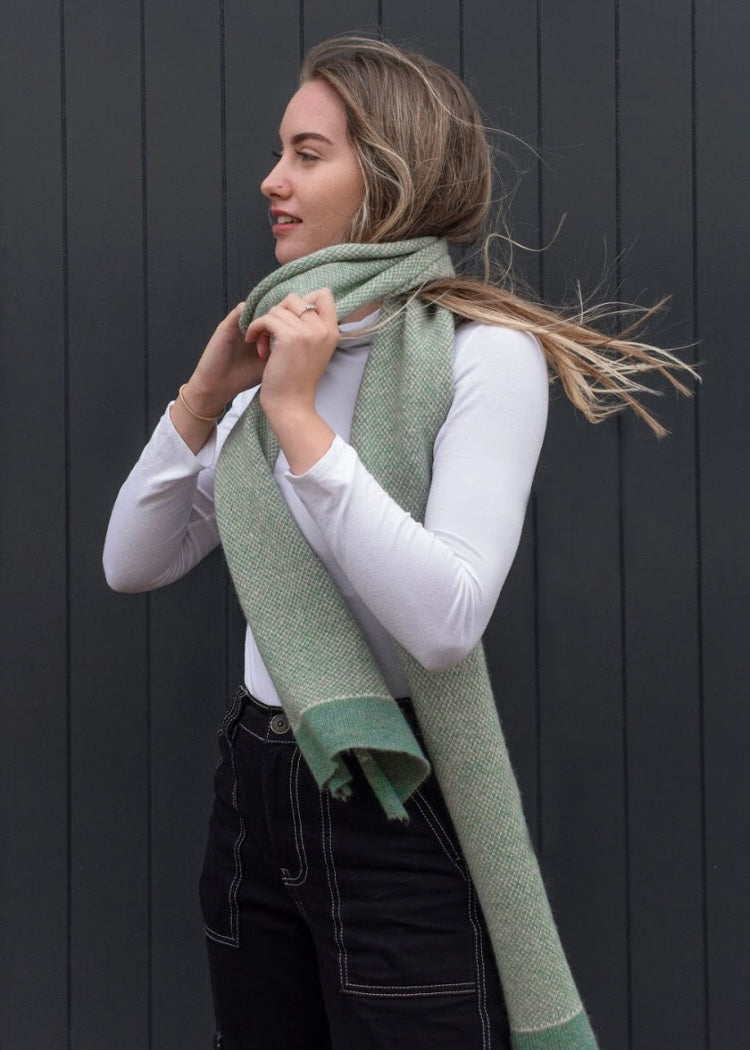 Woman wearing a knitted green scarf against a dark background