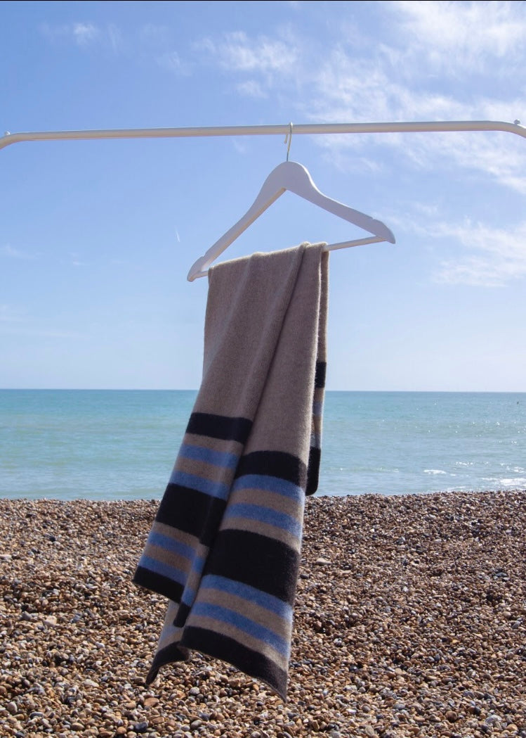 Striped knitted scarf on a hanger against a beach backdrop with ocean and sky.