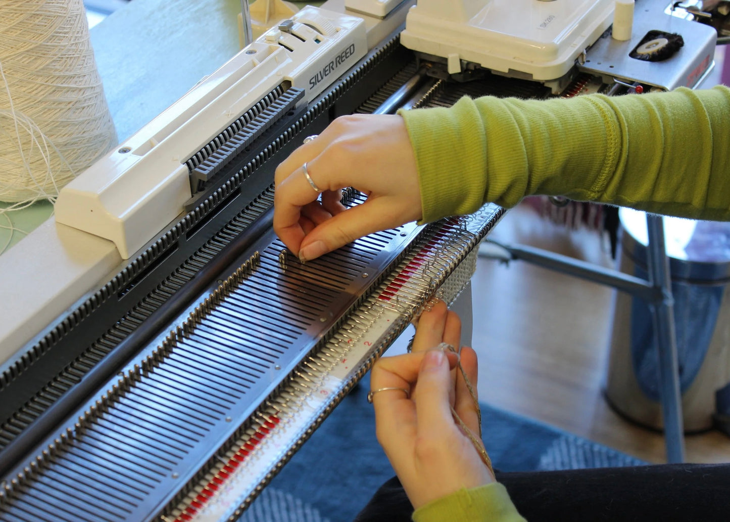 Person using a knitting machine with a focus on hands and equipment