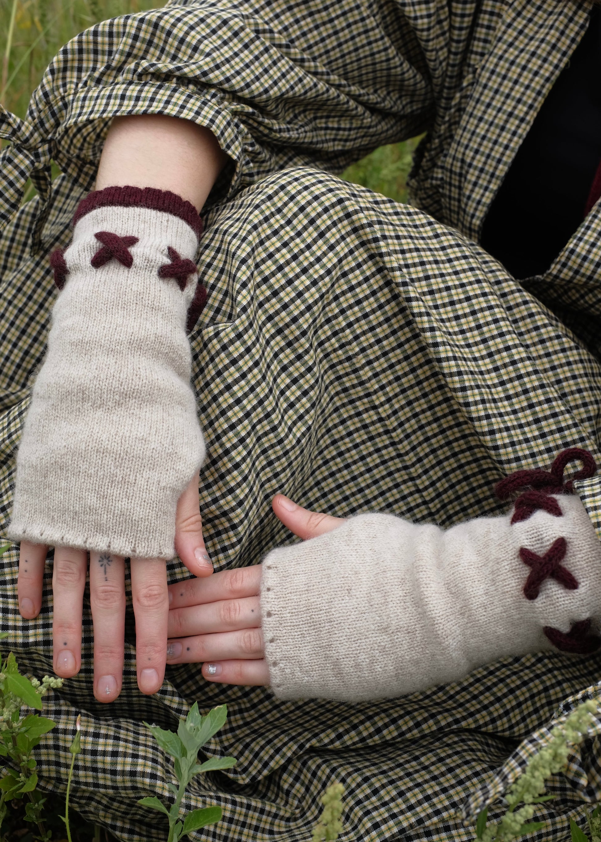Person wearing plaid clothing with knitted cream fingerless gloves featuring dark purple  accents.