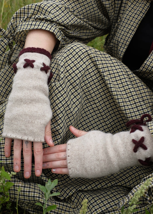 Person wearing plaid clothing with knitted cream fingerless gloves featuring dark purple  accents.