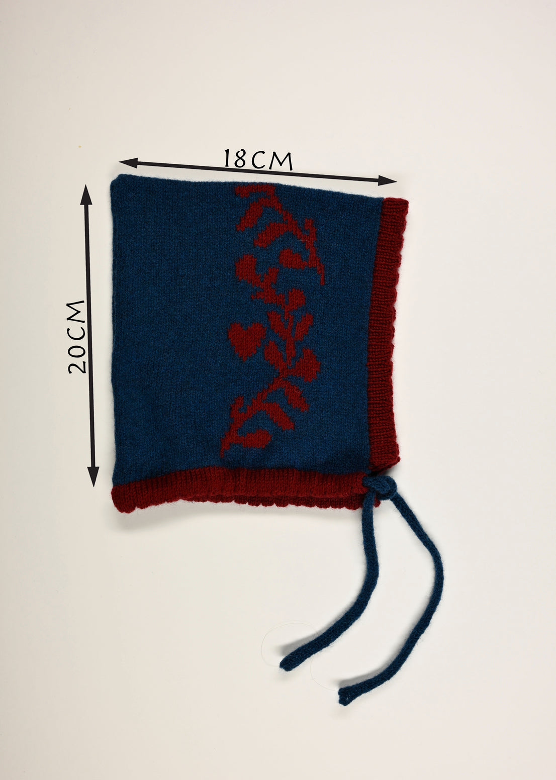 Blue and red knitted baby bonnet with measurements (20cm long by 18cm wide) on a white background