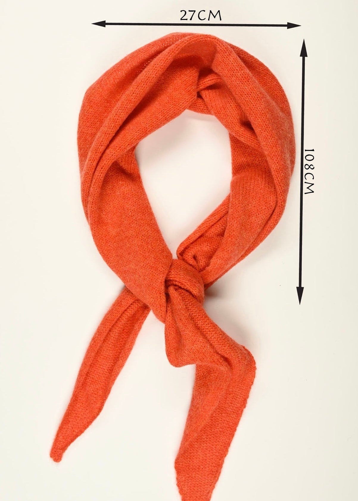 A flay lay of our orange cashmere knitted scarf tied neatly with two arrows demonstrating the size which is 108cm long by 27cm wide 