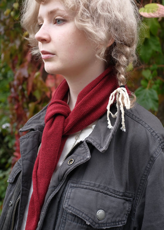 Person wearing a red scarf and dark jacket with braided hair, standing outdoors.
