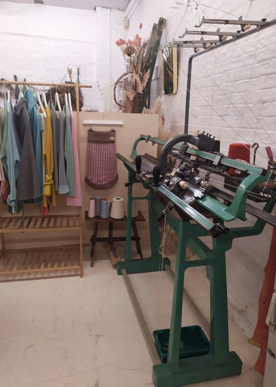 Clothing rack with clothes and a knitting machine in a workshop setting.