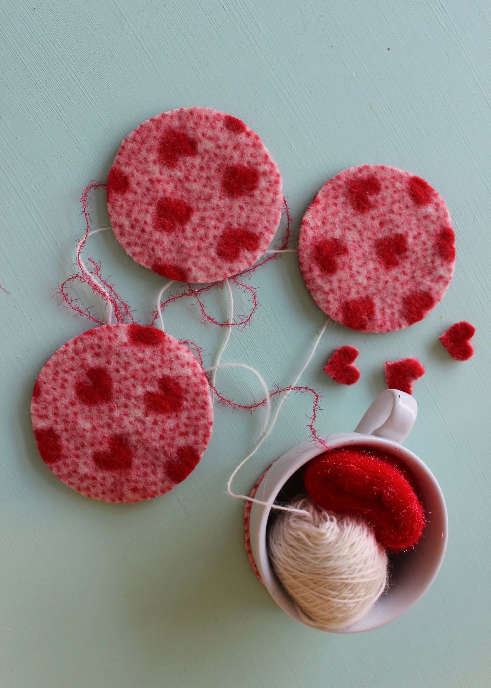 Red heart-shaped felt coasters with a cup of yarn on a light green background