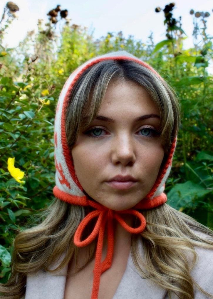 Woman wearing an orange and white hooded garment against a natural background