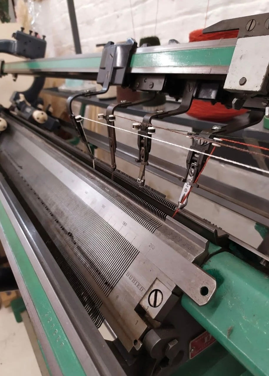 Close-up of a knitting machine with metal needles and green frame.