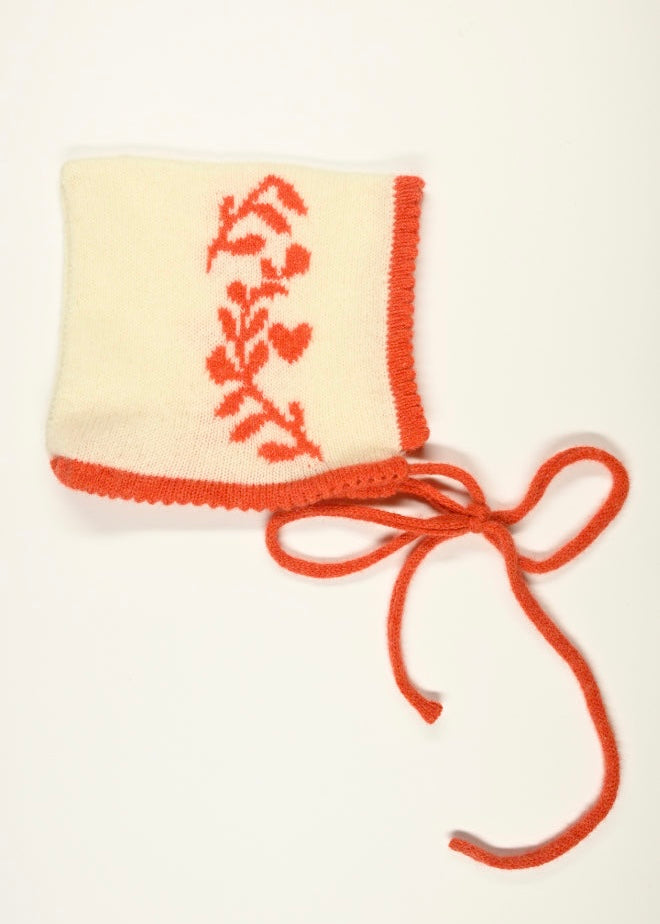 Knitted baby bonnet with orange floral laurel leaf design on a white background