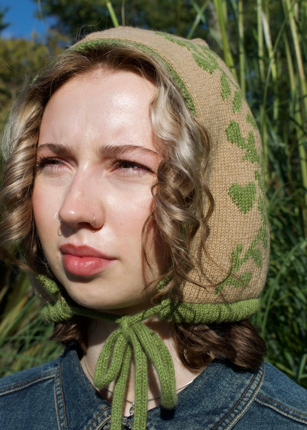Woman wearing a knitted green and tan bonnet against a natural background
