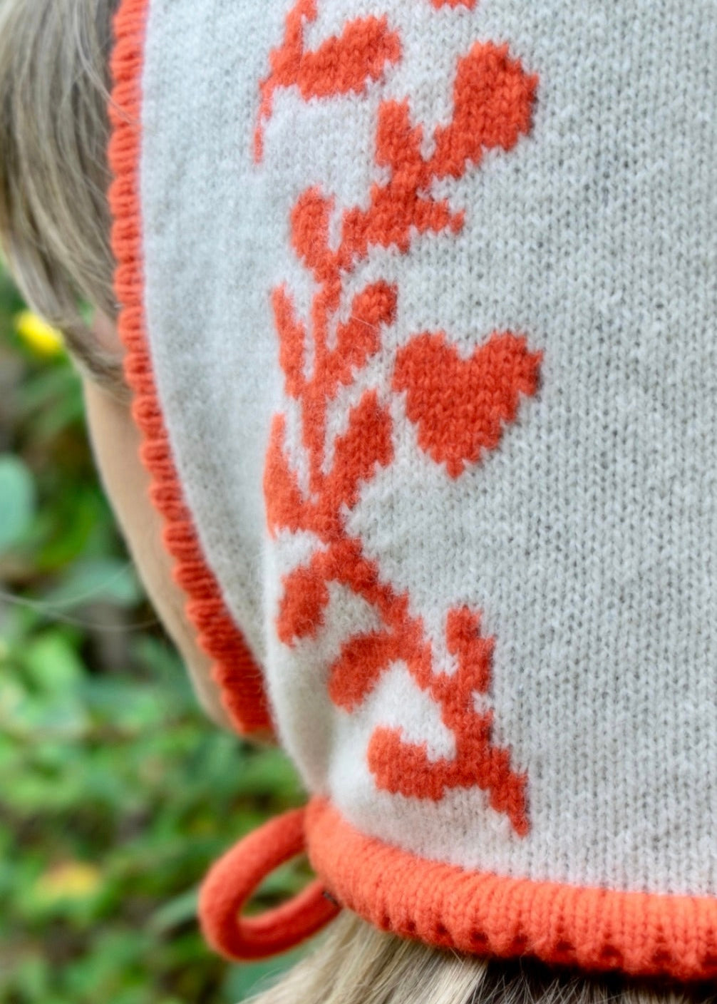 Close-up of a knitted glove with orange and white pattern against a blurred natural background