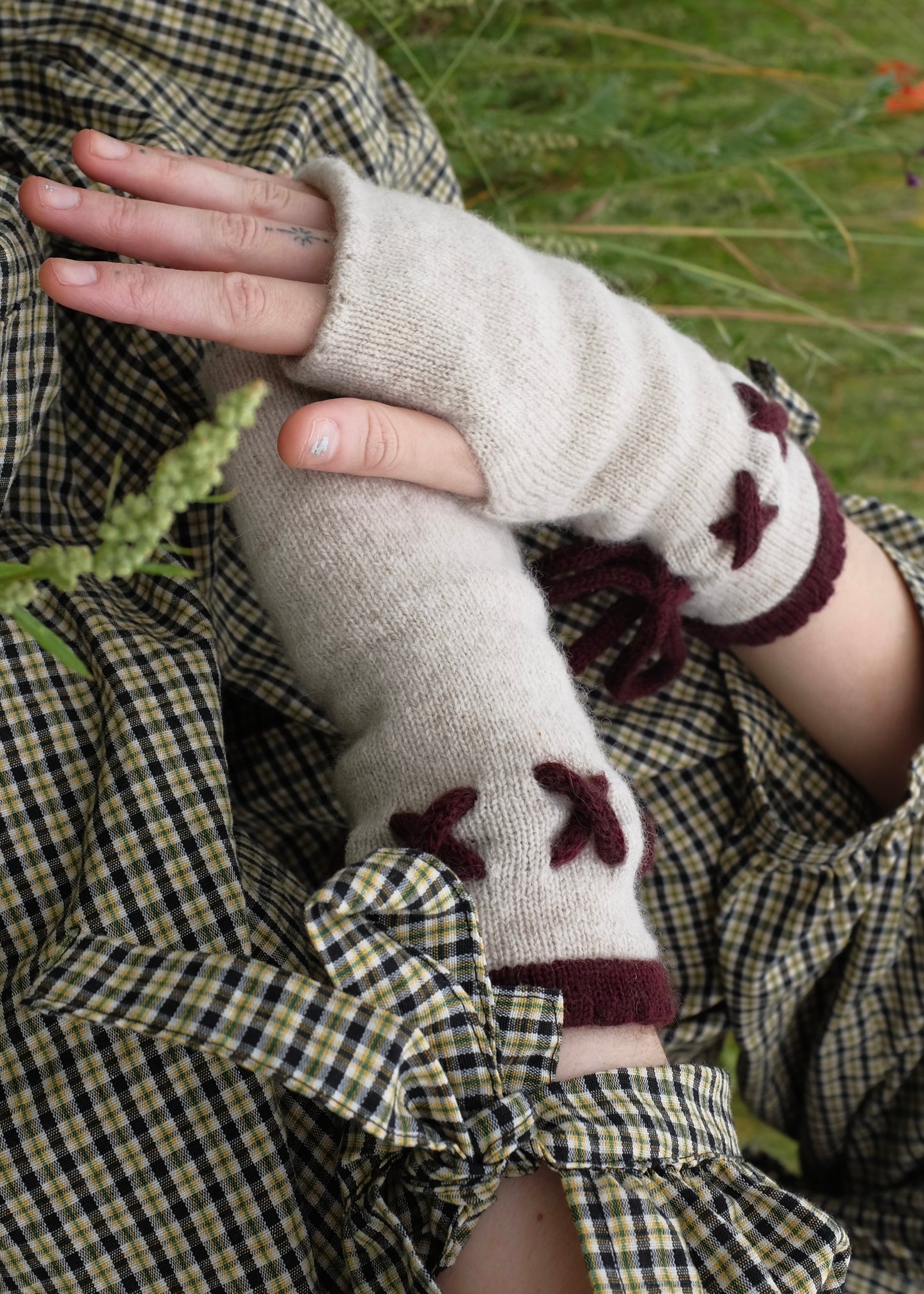 Person wearing fingerless gloves with a cream base and dark purple details in a natural setting