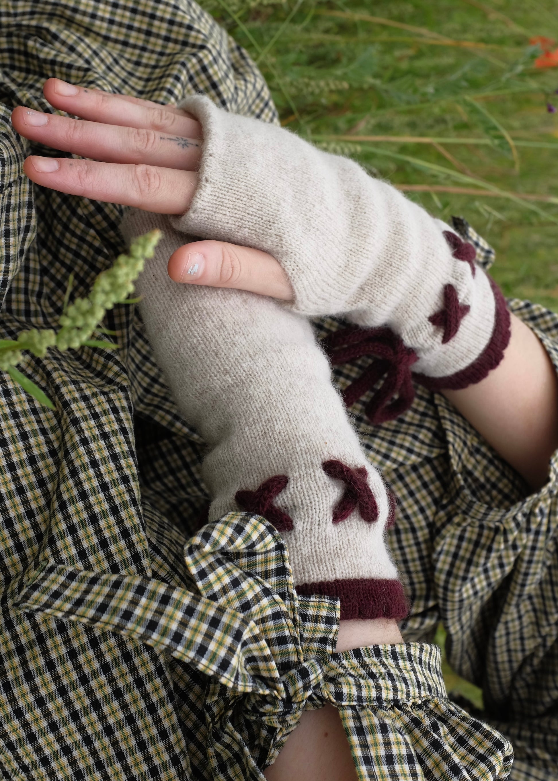 Person wearing fingerless gloves with a cream base and dark purple details in a natural setting