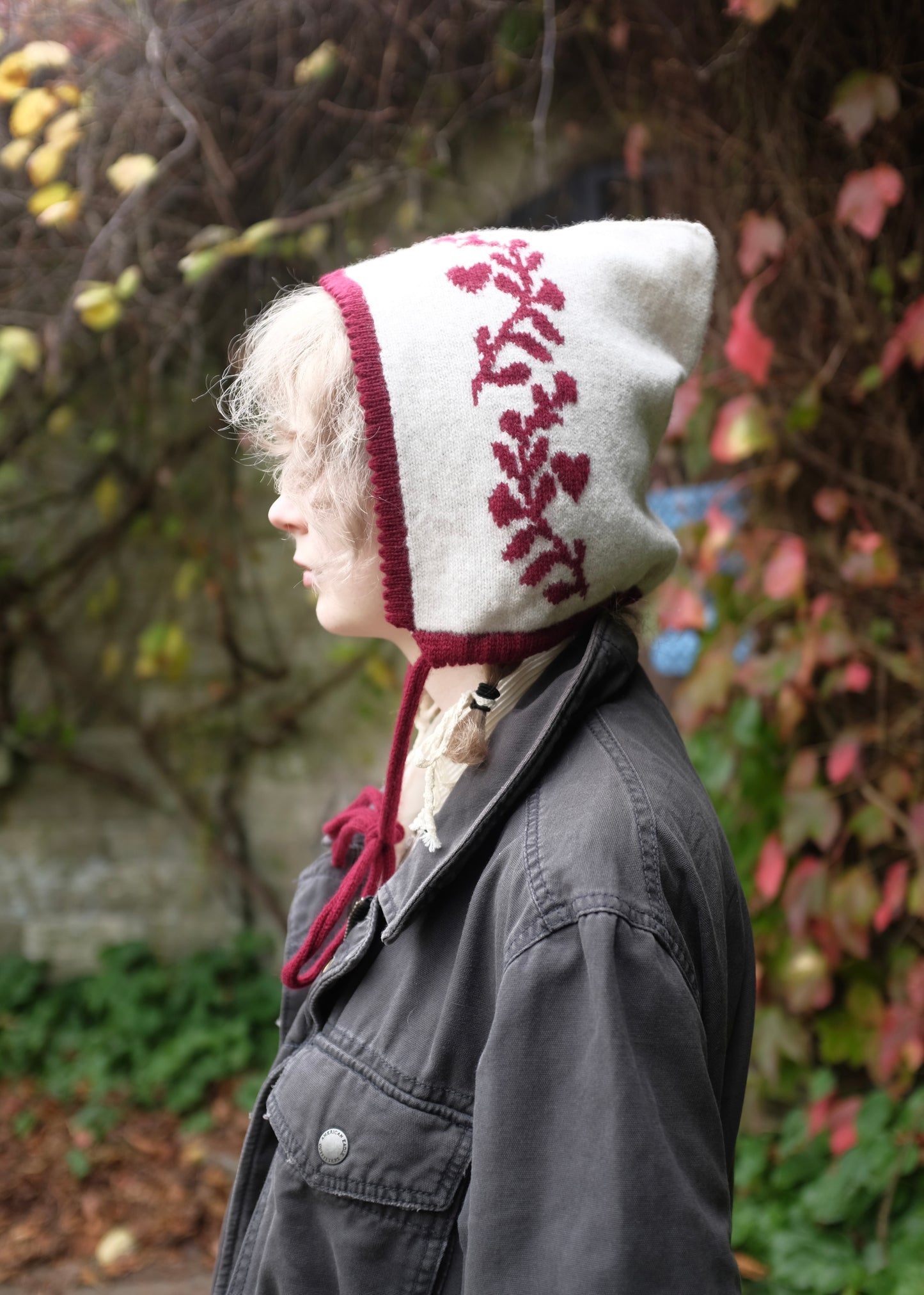 Person wearing a white knitted bonnet with red laurel leaf print in an outdoor setting.