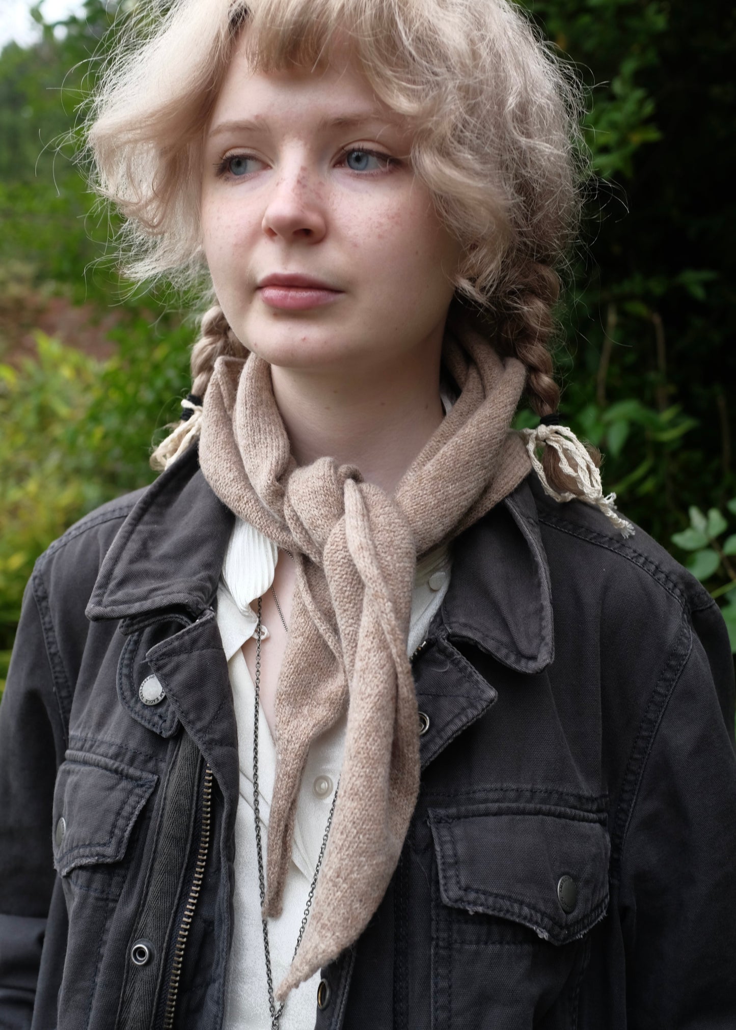 Person wearing a beige knitted chasmere scarf and dark jacket with a blurred natural background