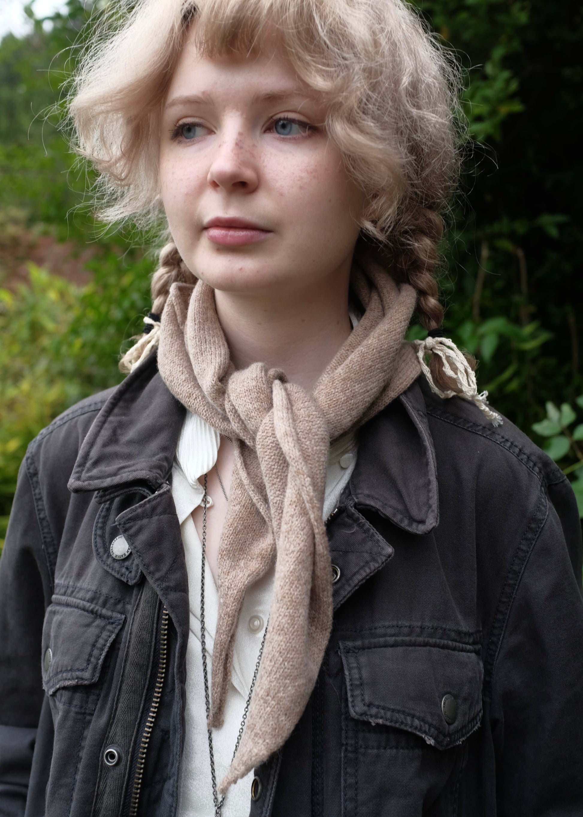 Person wearing a beige knitted chasmere scarf and dark jacket with a blurred natural background