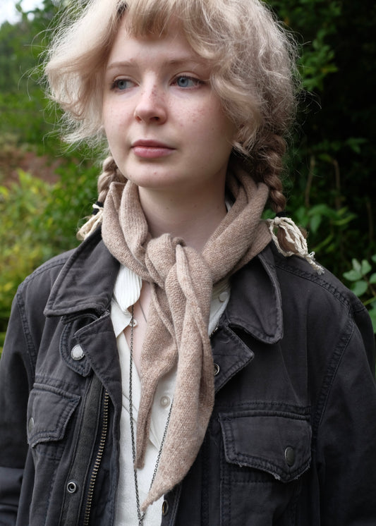 Person wearing a beige knitted chasmere scarf and dark jacket with a blurred natural background