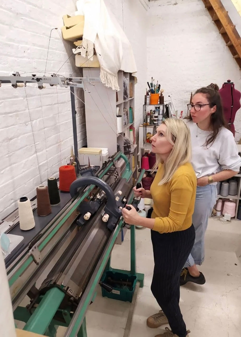 Two women working with textile equipment in a workshop setting.