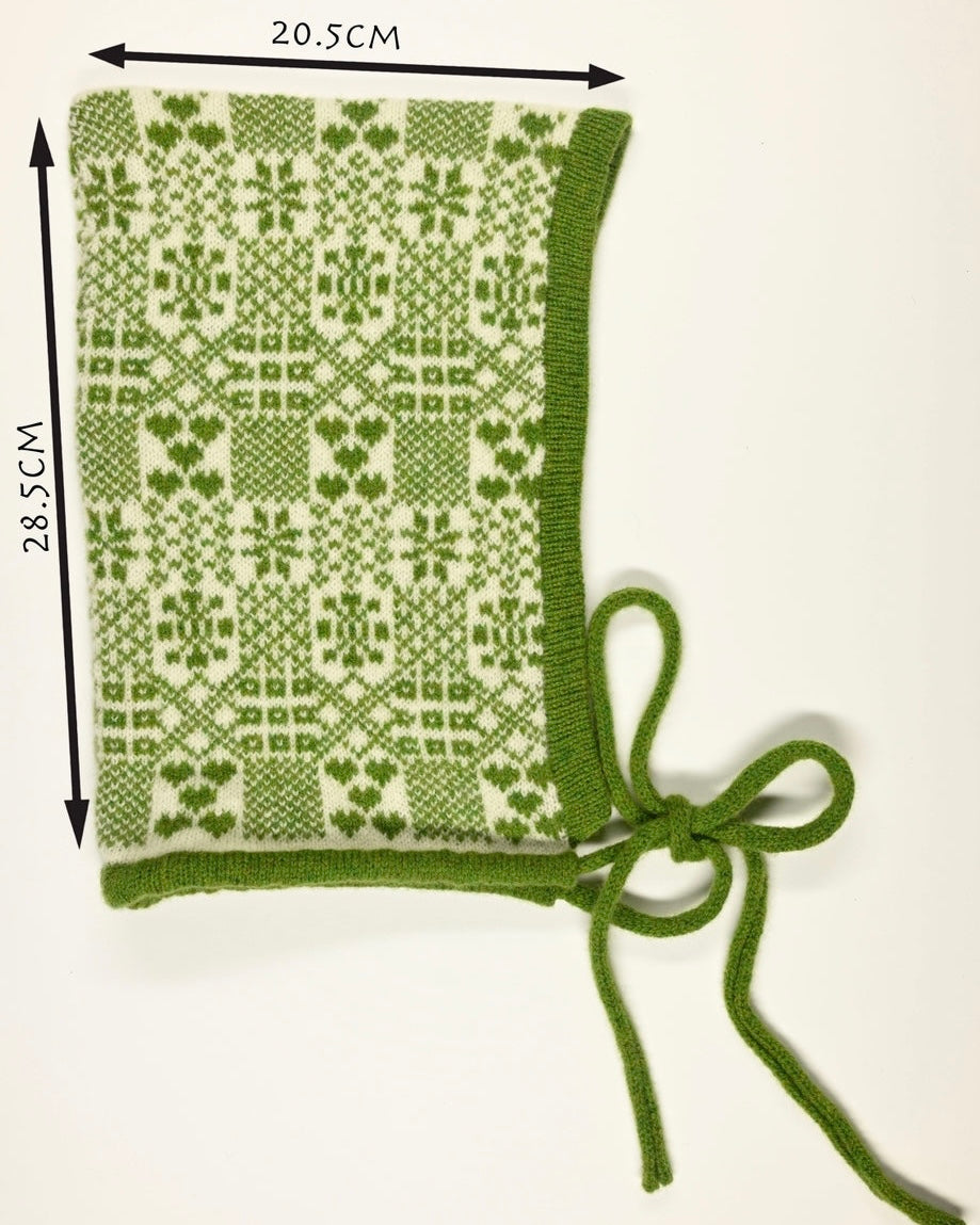 Green knitted bonnet with fair isle pattern and measurements (28.5cm long y 20.5cm wide) on a white background