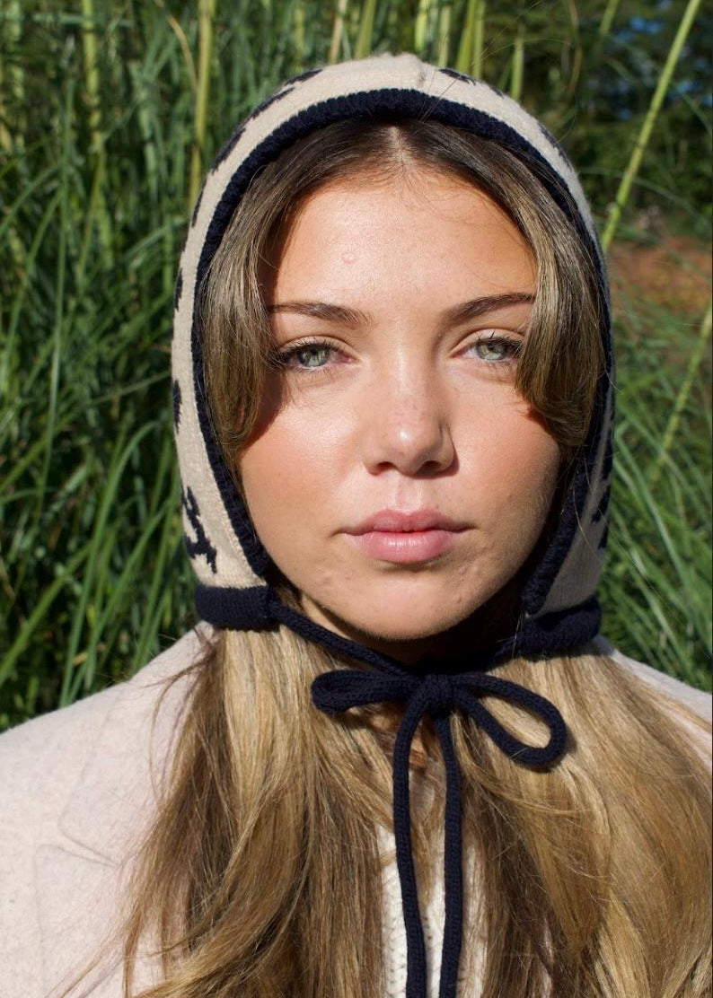Woman wearing a bonnet with a cream base and navy trim, pattern and bow tied neatly under her chin,  with a natural background