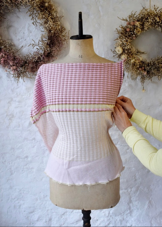 Person adjusting a knitted garment on a mannequin with a white and pink checkered top.