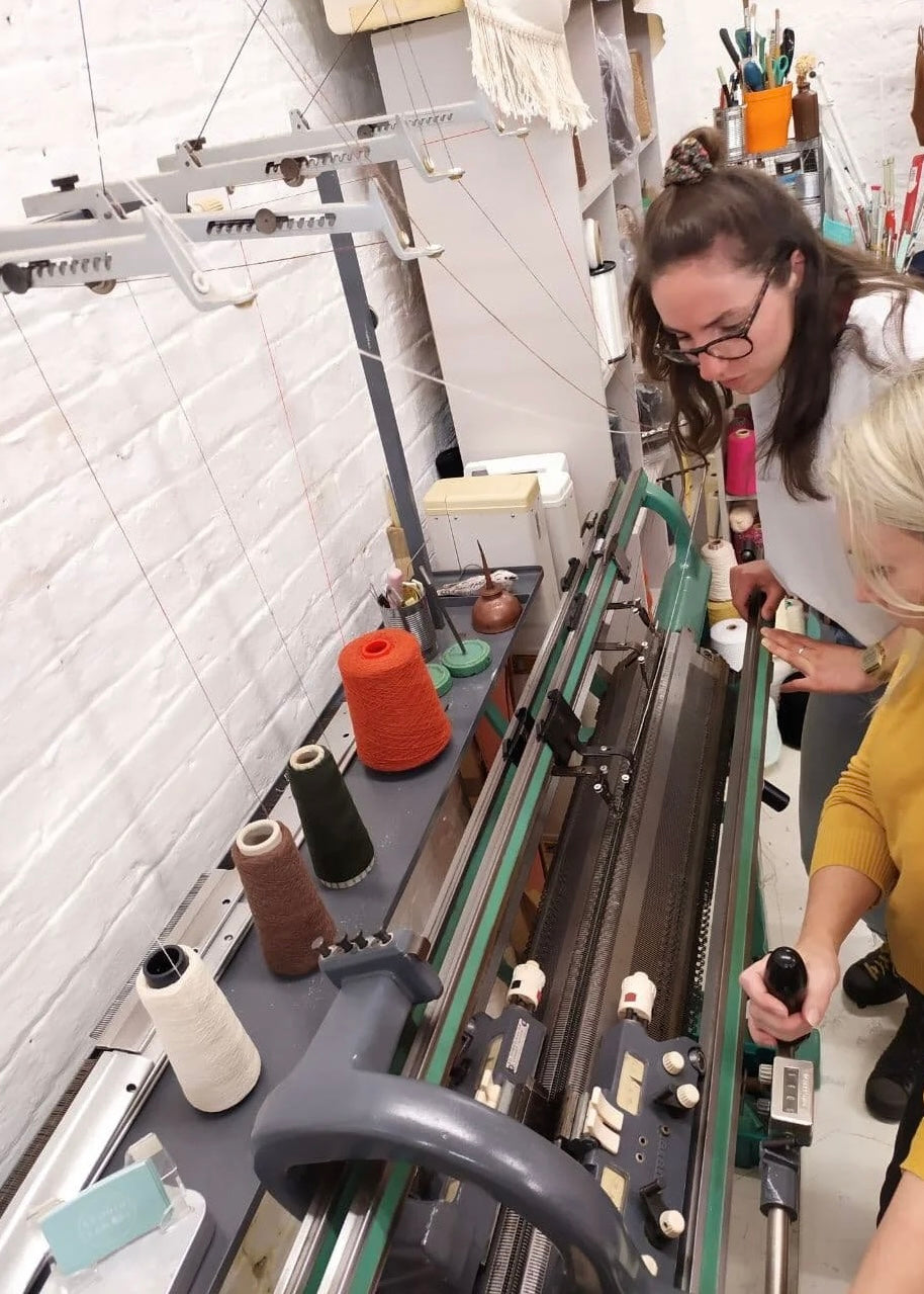 Two people working with a large knit machine in a workshop setting.
