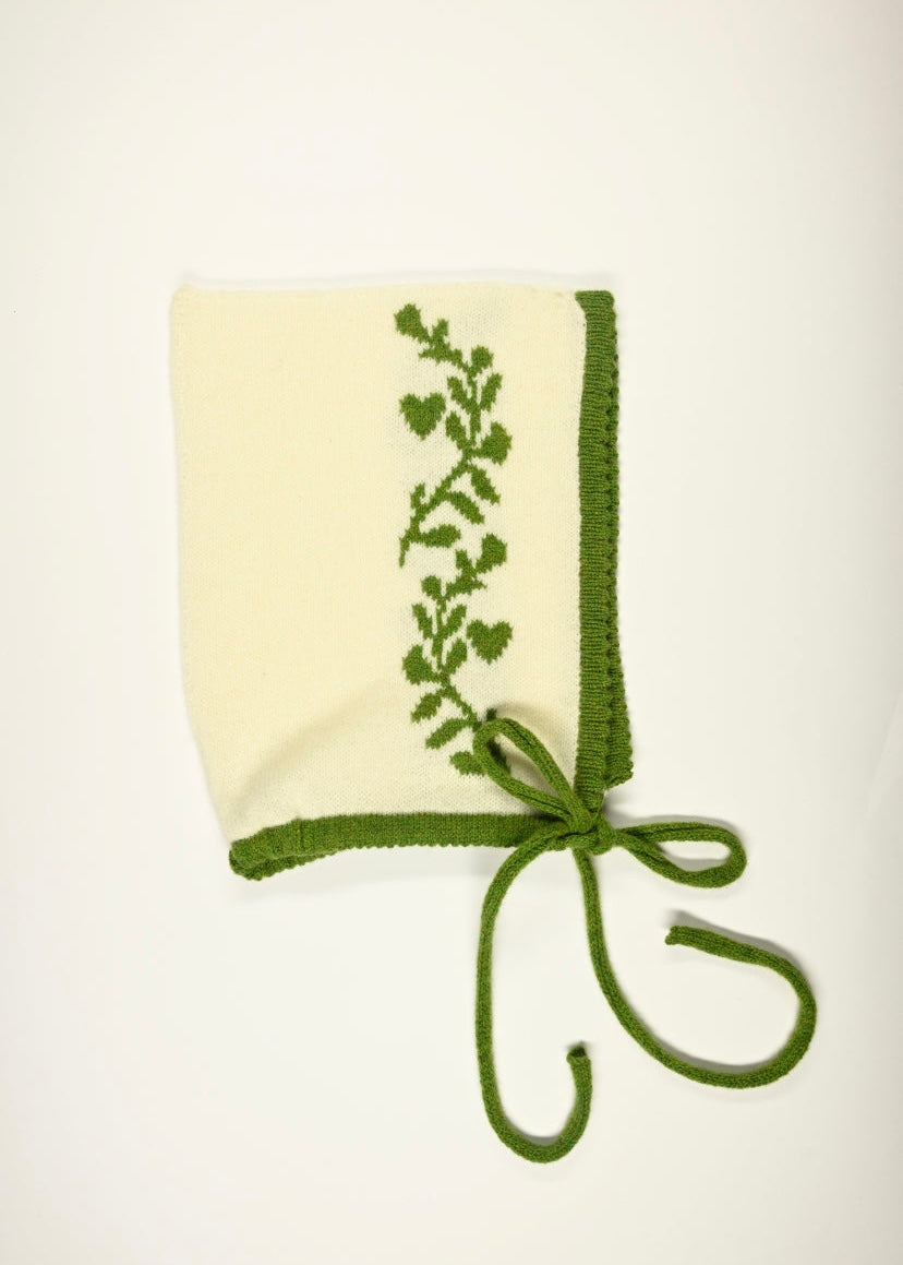 Cream bonnet with green floral  design on a white background