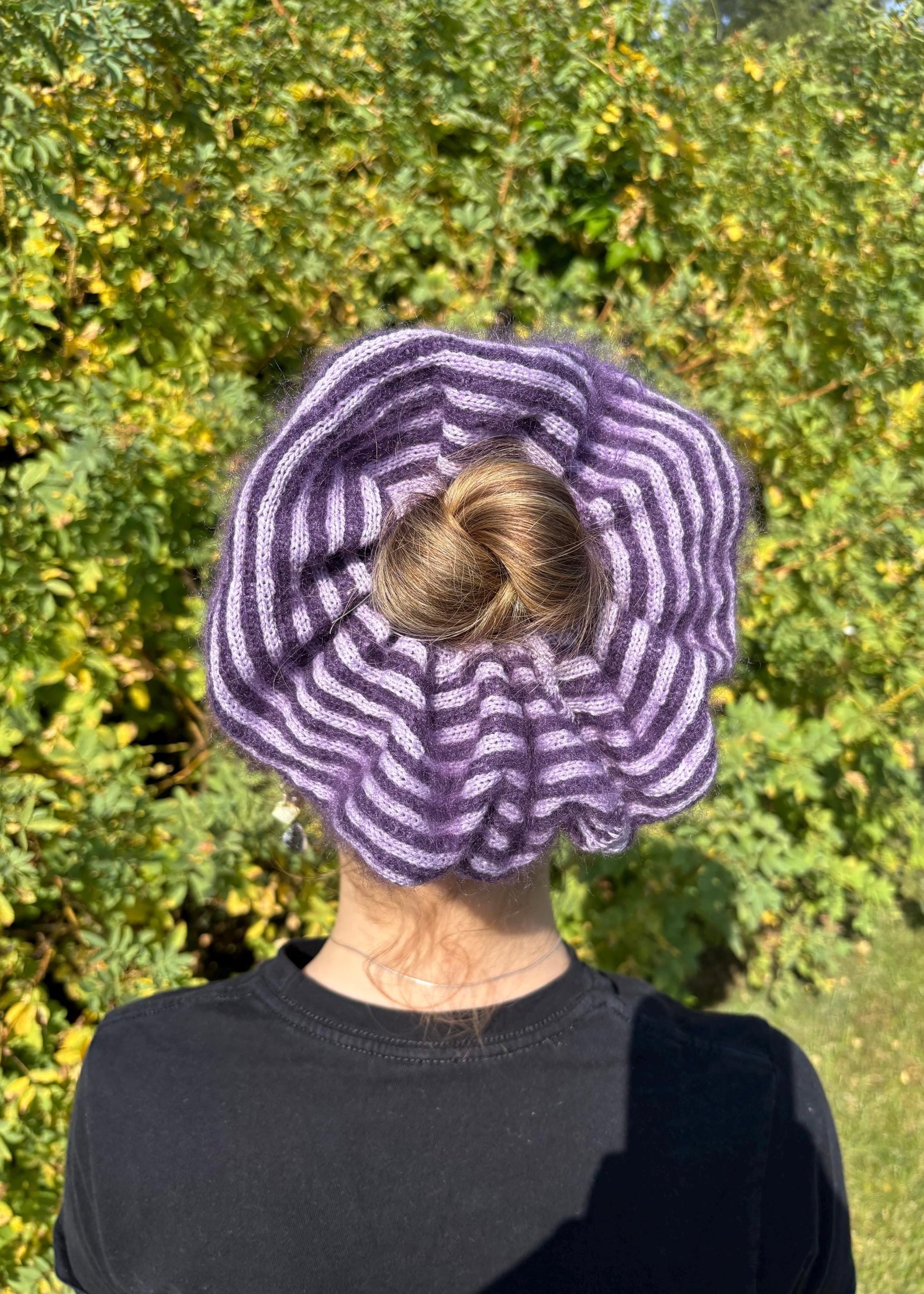Person wearing a dark purple and lilac striped  knitted  mohair scrunchie  outdoors.