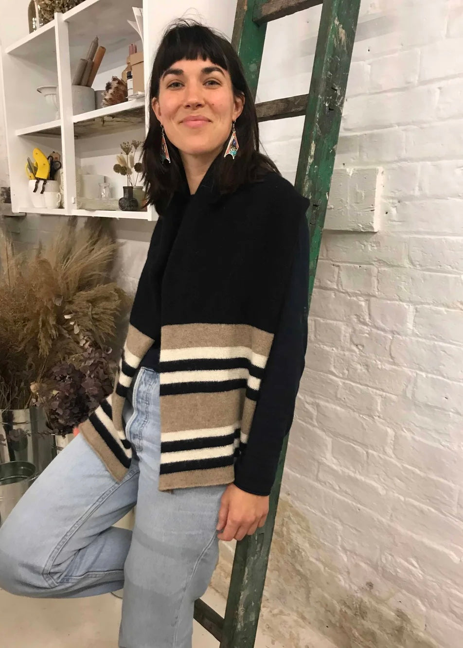 Person wearing a black, beige, and brown striped knitted scarf in a room with a white brick wall.