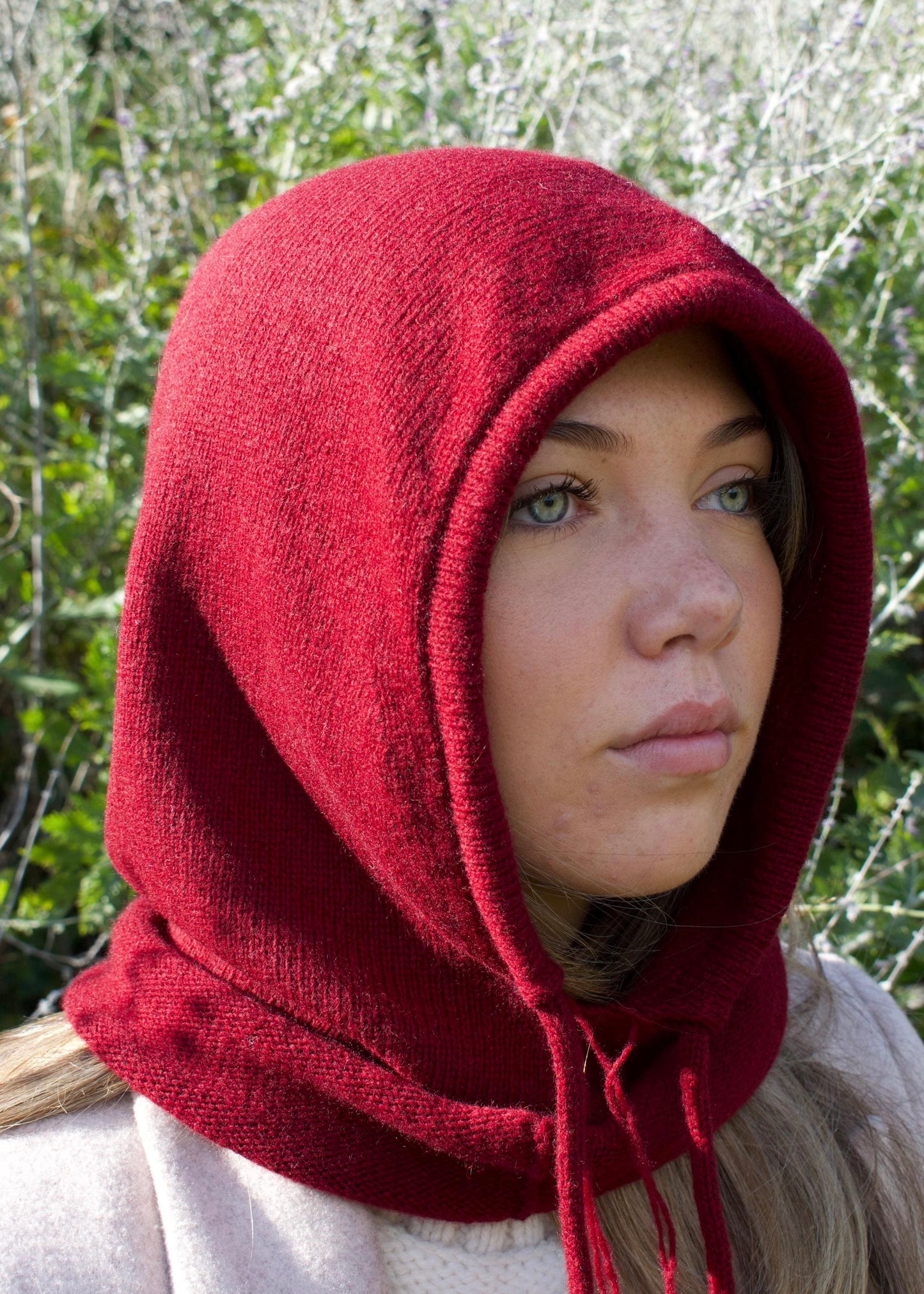 Our cashmere knitted balaclava hood in burgundy pictured on a woman from a side angle outdoors 
