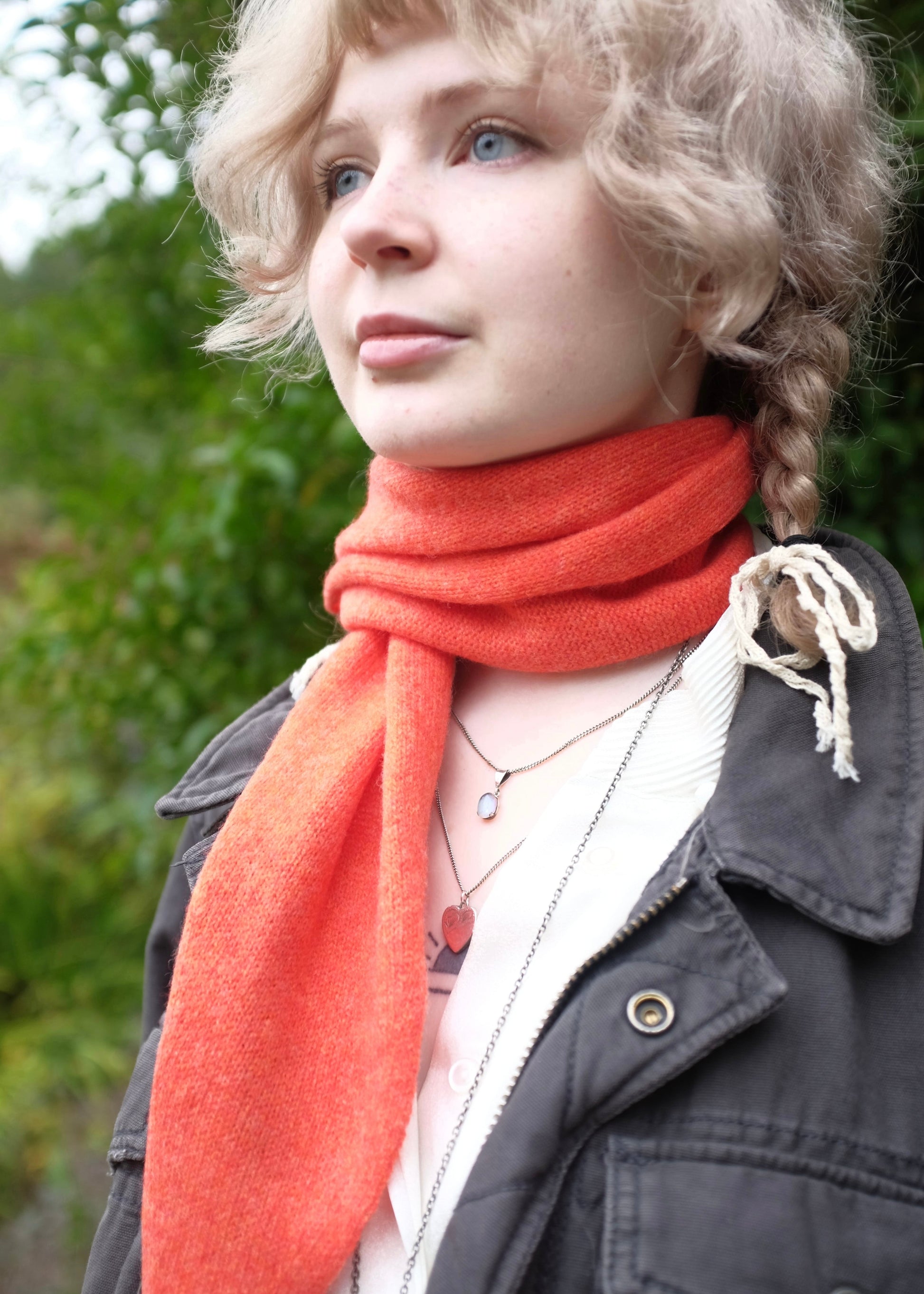 Person wearing an orange scarf draped around a woman’s neck on to her shoulder with a blurred green background
