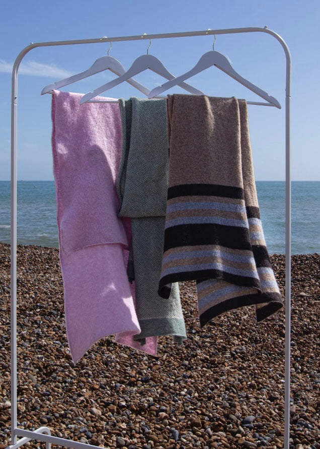 Three knitted scarfs hanging on a rack by the sea