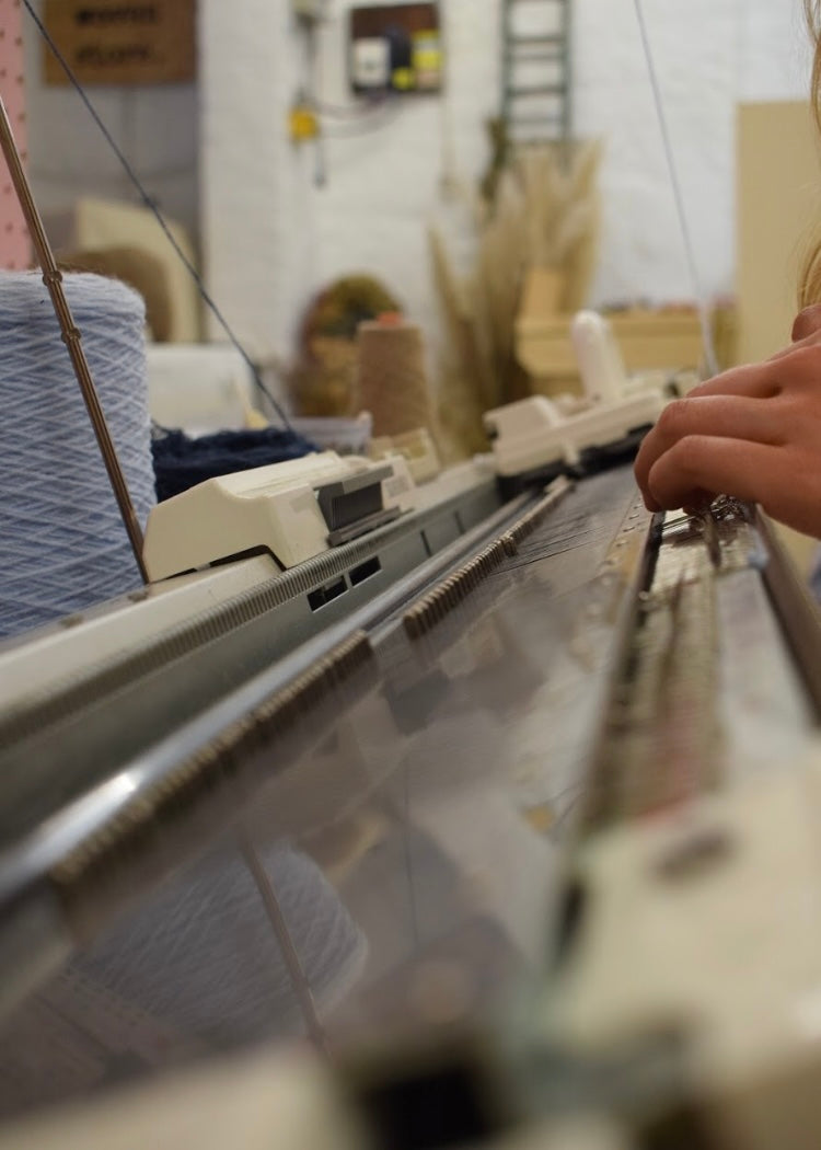 Close-up of a knitting machine with yarn and a person's hand in a blurred indoor setting