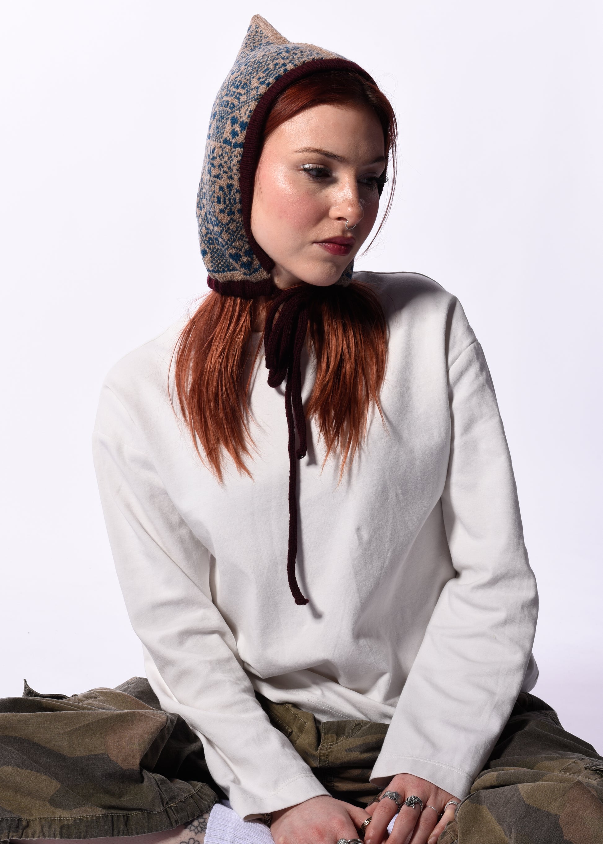 Person wearing a white hoodie and patterned bonnet on a plain background