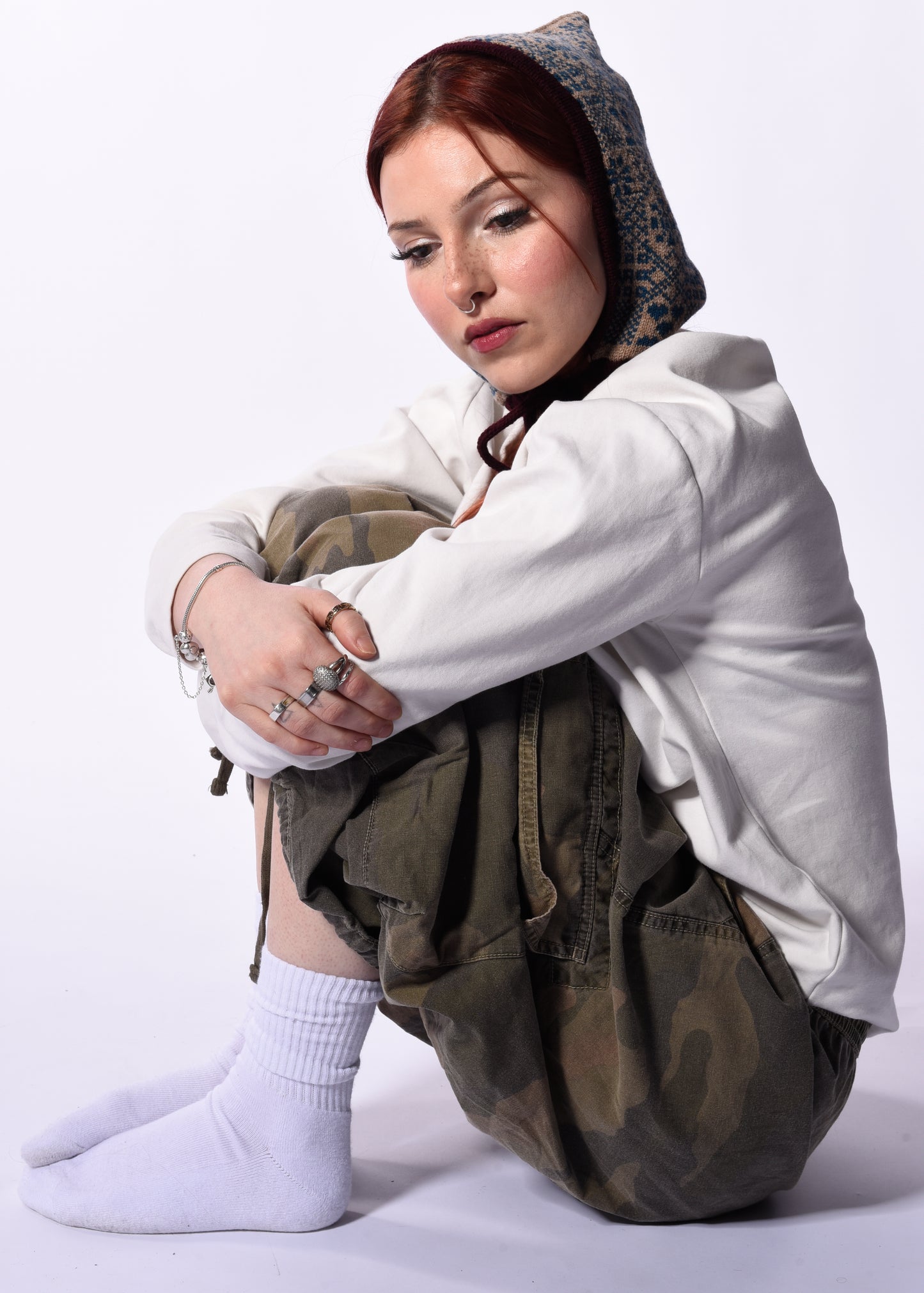 Person wearing a white hoodie and camouflage pants sitting on a white background