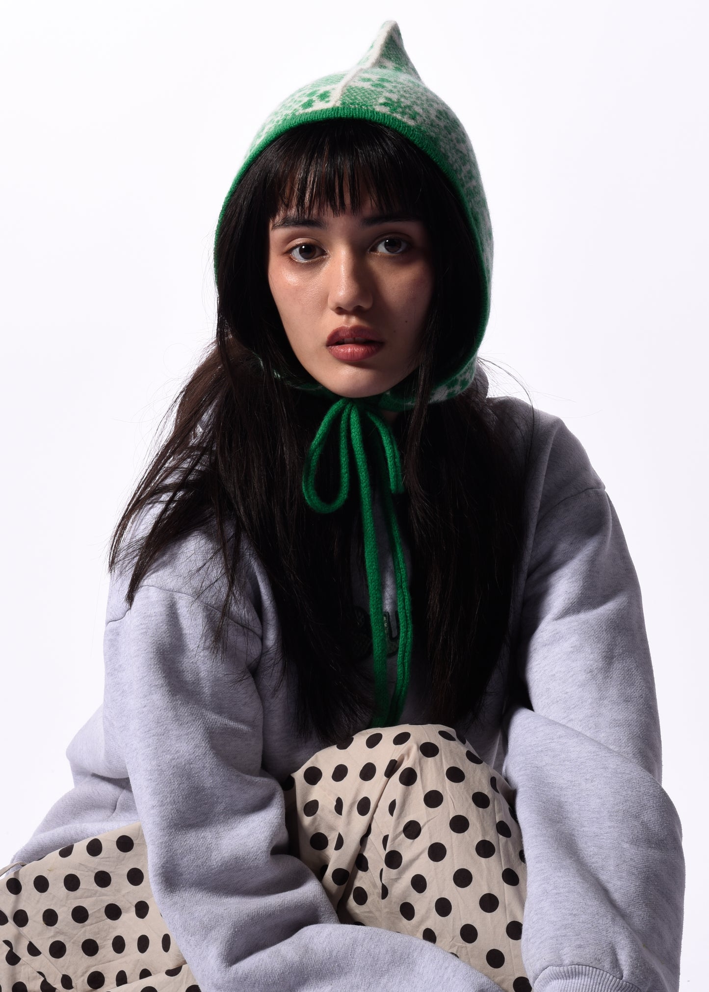 Person wearing a green bonnet with polka dot pants on a white background