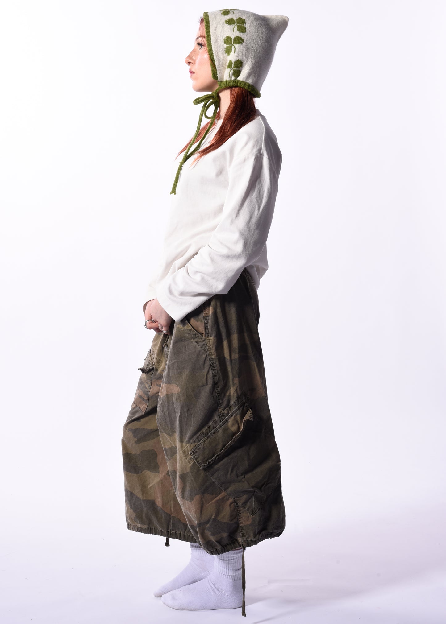 Person wearing a long green coat and white hoodie with a bonnet on a white background
